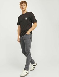 Černé tričko s krátkým rukávem s malým potiskem na kapse, spárované se šedými slim-fit džíny a bílými teniskami s černými akcenty.