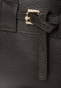 Brązowa skórzanka z fakturą z detalem w postaci zapięcia na klamrę. Posiada złote okucia i kontrastowe przeszycia. Zbliżenie podkreślające materiały.