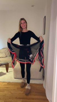 Sort og rød mønstret letvægts tørklæde holdt af en person, med logoaccents og et flydende design, vist mod en lys baggrund.