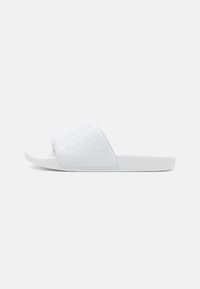 Hvide slidesandaler med en tekstureret overdel, der har et quiltet mønster og et åbent tå-design. Sålen er flad og let polstret.