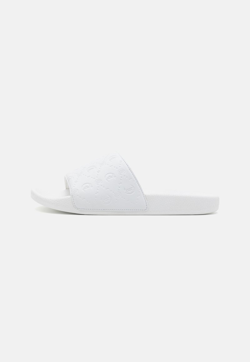 Hvide slidesandaler med en tekstureret overdel, der har et quiltet mønster og et åbent tå-design. Sålen er flad og let polstret.