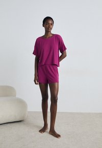Māršala loungewear komplekts, kas sastāv no īsa, īsām piedurknēm T-kreklam un atbilstošām šortiem ar auklu un pogu detaļām. Mīksta auduma tekstūra.