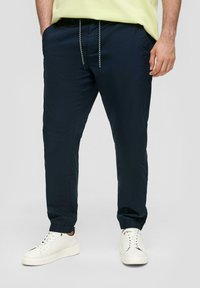 Granatowe spodnie dresowe z lekkiego materiału, z elastycznymi mankietami, wyposażone w rozciągliwy pas oraz boczne kieszenie, zestawione z białymi tenisówkami.
