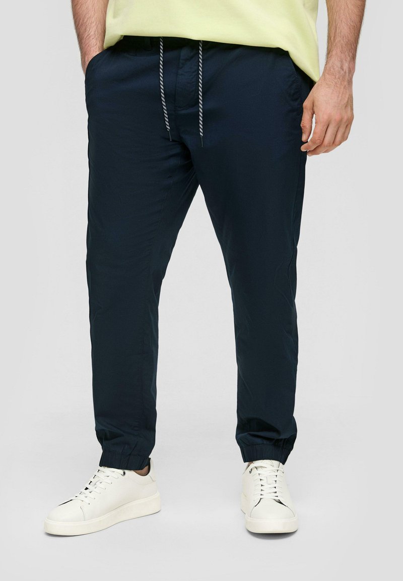 Granatowe spodnie dresowe z lekkiego materiału, z elastycznymi mankietami, wyposażone w rozciągliwy pas oraz boczne kieszenie, zestawione z białymi tenisówkami.