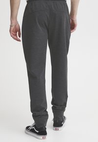 Pantalones deportivos grises con un acabado texturizado, que presentan una cinturilla elástica, bolsillos traseros y un diseño de pierna entallada. Combinados con zapatillas negras.
