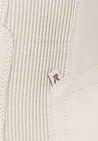 Botín de cuero blanco con textura acanalada, costuras visibles y una pequeña etiqueta que muestra la letra "R". Acabado suave con diseño estructurado.