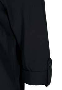Manga de camisa negra de algodón, con un puño enrollado que presenta un detalle de botón. Textura suave con costuras uniformes y sin patrones visibles.