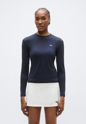 Tumesinine pika varrukaga spordipluus ümmarguse kaelusega ja istuva lõikega, kombineeritud valge seelikuga, millel on must logotriip. Sile tekstuur.