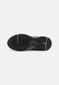 Black rubber athletic shoe sole with a textured hexagonal pattern and grooves for traction, featuring a beige accent along the edge.