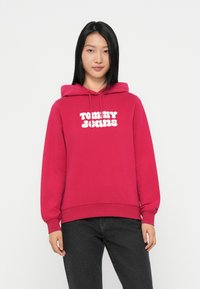 Sweatshirt à capuche fuchsia en mélange de coton. Pr�ésente le logo "TOMMY JEANS" en blanc. Manches et ourlet côtelés. Associé à un jean foncé.