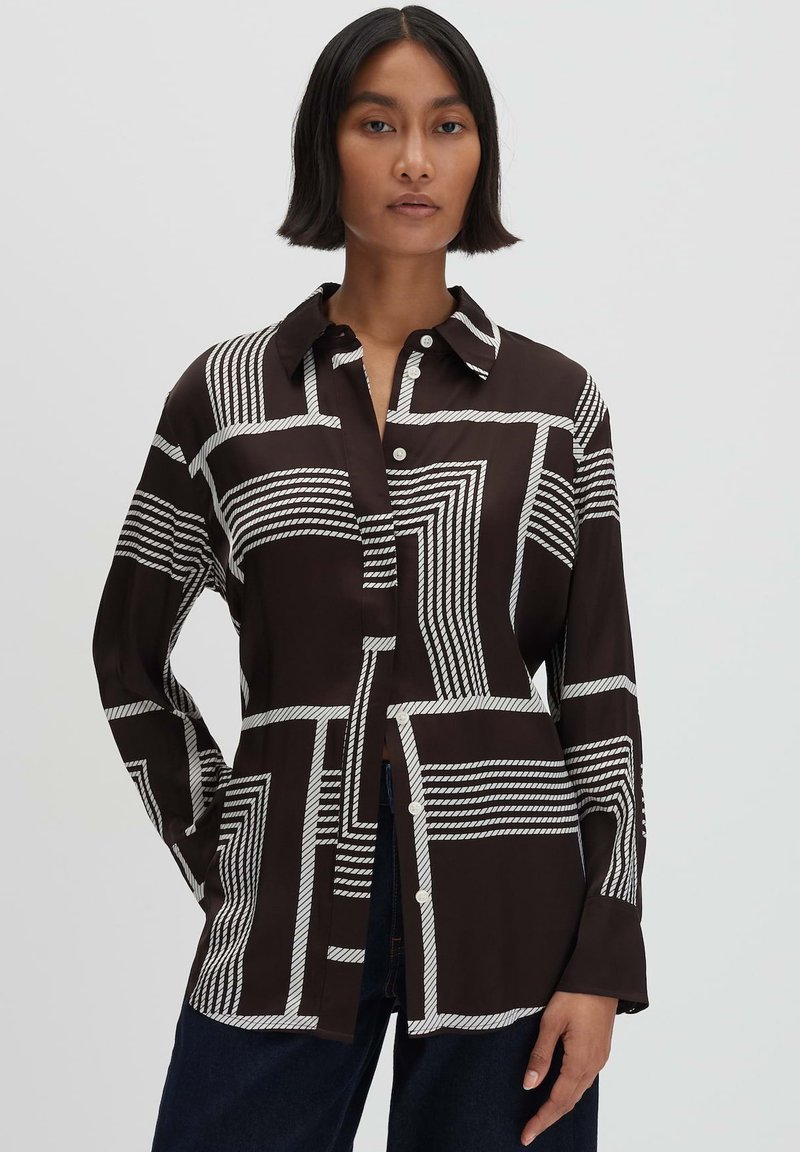 Camicia a maniche lunghe con bottoni di colore marrone scuro, decorata con motivi geometrici bianchi. Presenta un colletto e una vestibilità rilassata con spacco laterale.