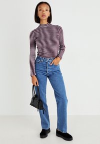 Striped long-sleeve top in burgundy and white, paired with high-waisted blue jeans. Black handbag and dark shoes complete the look.
