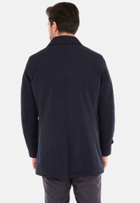 Cappotto blu navy con taglio dritto, tasche anteriori e collo a rever. Realizzato in tessuto strutturato, presenta una cucitura visibile lungo la schiena.