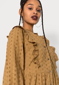 Vestido castanho, texturado, com bordados florais, colarinho e mangas com volantes, fecho de botão e saia em camadas.