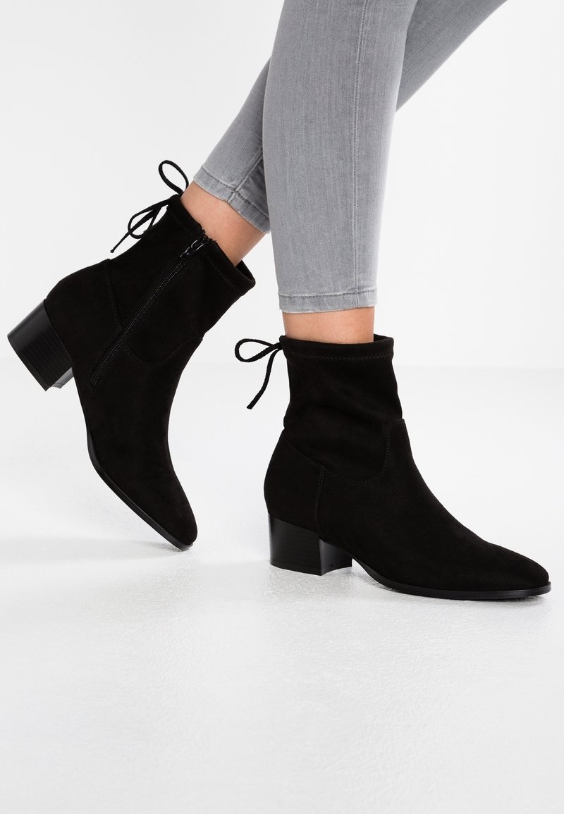 Bottines en daim noir avec fermeture zippée et détail nœud, dotées d'un petit talon bloc et d'une texture lisse.