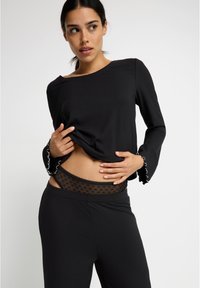 Haut noir à manches longues côtelé avec des poignets volantés, assorti à un pantalon de détente noir avec une taille en tulle à pois.