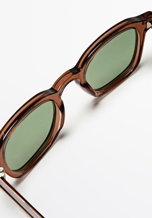 Bruine doorschijnende rechthoekige zonnebril met groen getinte glazen tegen een witte achtergrond.