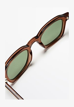 Bruine doorschijnende rechthoekige zonnebril met groen getinte glazen tegen een witte achtergrond.