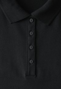 Svart polo t-shirt med en texturerad krage och en knappslå med fem svarta knappar. Tyget ser slätt och lätt ut.