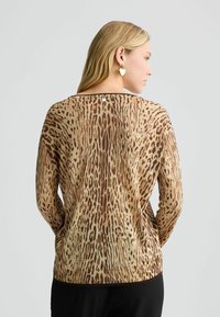Maglia a maniche lunghe color tan con stampa leopardata marrone. Presenta un collo a barca, un orlo a costine e un delicato dettaglio con bottone sulla schiena.