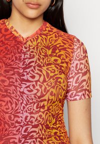 Top justo de mangas curtas com um padrão degradê em vermelho, laranja e amarelo, com uma textura suave e ligeiramente translúcida.
