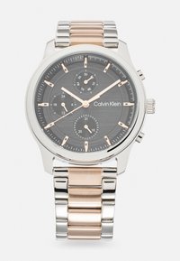 Reloj cronógrafo en plata y oro rosa con esfera negra texturada, tres subesferas y pantalla de fecha. Presenta una pulsera de eslabones metálicos.