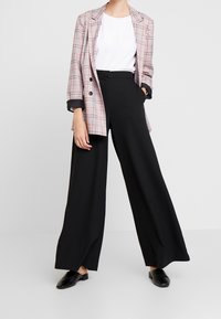 Rutigt kavaj med svarta accenter, vit skjorta och vida svarta byxor. Slät textur, skräddarsydd passform och korta ärmar framhäver designen.