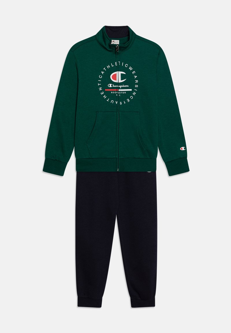 Chaqueta verde con cierre, con logo blanco, combinada con pantalones de chándal negros. Ambos hechos de material suave, con puños elásticos y bolsillos.