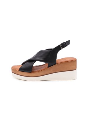 Sandali platform in pelle nera con design a fascette incrociate, sottopiede imbottito color beige e suola in gomma bianca. Accentatura della fibbia in argento sulla fascetta.