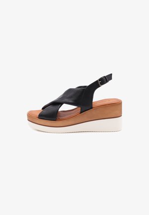 Sandali platform in pelle nera con design a fascette incrociate, sottopiede imbottito color beige e suola in gomma bianca. Accentatura della fibbia in argento sulla fascetta.