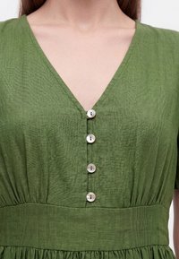 Close-up of a green V-neck dress with four white buttons down the front and a wide waistband.