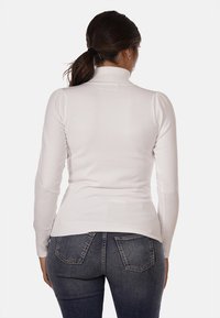 Maglione bianco a collo alto con maniche lunghe aderenti e orlo a coste. Tessuto a maglia texturizzato con una finitura liscia, indossato con jeans di denim scuro.