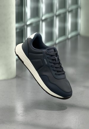 Marineblaue Sneaker mit texturierter Oberseite, weißer Gummisohle und schwarzen Akzenten. Verfügt über Schnürsenkel und Markenlogo an der Seite.