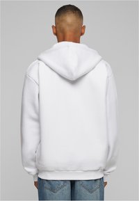 White hoodie with a drawstring hood, ribbed cuffs, and hem, paired with blue denim pants. Smooth texture with a relaxed fit.