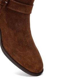 Stivale alla caviglia in suede marrone con punta affusolata, piccolo dettaglio a strappo e superficie liscia e testurizzata. Presenta una suola in gomma scura.