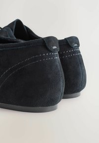 Scarpe in suede nere con tacco basso, caratterizzate da dettagli cuciti e una forma liscia e curvata nella parte posteriore.