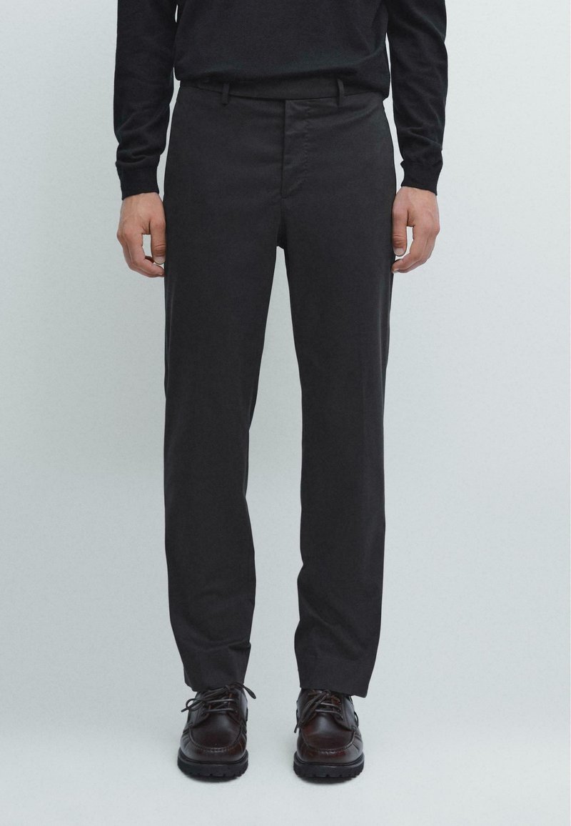 Černé kalhoty na míru vyrobené z hladkého materiálu, s rovným střihem, přičemž na přední straně mají sklad a nenápadné bokové kapsy.