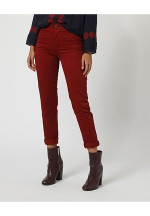 Pantalones de algodón rojo con un ajuste slim y dobladillos enrollados, combinados con botas de tobillo marrón oscuro con cremallera lateral y tacón de bloque.