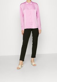 Rosa Satinhemd mit Knopfleiste und langen Ärmeln, kombiniert mit schwarzen tapered Pants und hellbeigen offenen Schuhen mit Absatz. Glatte Textur und lockere Passform.