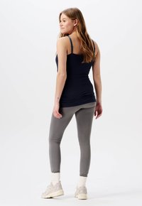 Marinblå linne med justerbara remmar, parat med ljusgrå leggings. Texturen är slät och passformen är figurnära. Tillbehören inkluderar ljusa skor.