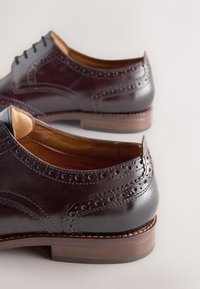 Chaussures en cuir bordeaux foncé avec des détails brogue, une finition lisse, un bout arrondi et un talon empilé marron. Design classique à lacets.