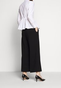 Blusa peplum bianca con vita arricciata, abbinata a pantaloni neri a gamba larga e tacchi a punta neri. Tessuti lisci e strutturati.