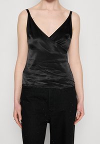 Svart satin camisole med V-ringning och inlindningsdesign, med tunna spännen och en mjuk textur. Matchas med svarta jeans prydda med nitar.