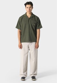 T-paita lyhyillä hihoilla, tummanvihreä, tekstuuri-kangas, avonainen kaulus ja rintatasku. Yhdistetty vaaleanbeigeihin, leveälahkeisiin housuihin.