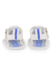 Sandalias blancas con rayas azules, diseño abierto y suela interior texturizada. Cuentan con una correa segura y un patrón de logotipo en azul.