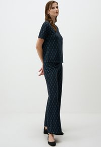 Korte mouwen top en wijde broek in donkere stof met een geometrisch patroon in teal en zwart, zachte textuur en een relaxte pasvorm.