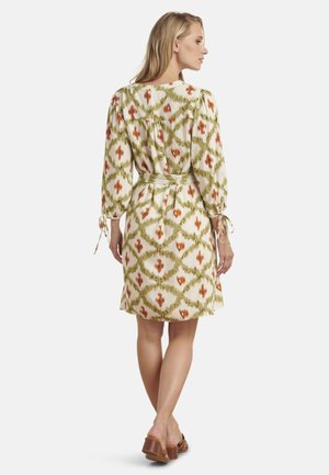 Kantine bloemendessin jurk in crème, groen en oranje. Heeft lange mouwen en een strik taille. Glad materiaal met een ontspannen pasvorm.