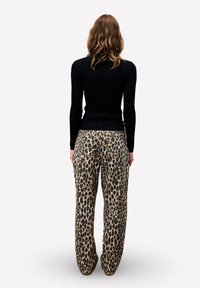 Zwarte geribbelde longsleeve top gecombineerd met losse, met luipaardprint bedekte broeken met een zachte textuur en zakken, bekeken vanuit de achterkant.