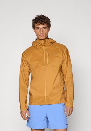Lightweight, hooded jacket in mustard yellow, made of water-resistant material. Features a zippered front and logo detail on the chest.