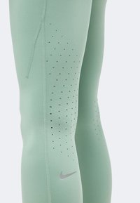 Ανοιχτό πράσινο αθλητικό κολάν με διάτρητες οπές αερισμού και μικρό ανακλαστικό λογότυπο Nike στη γάμπα.